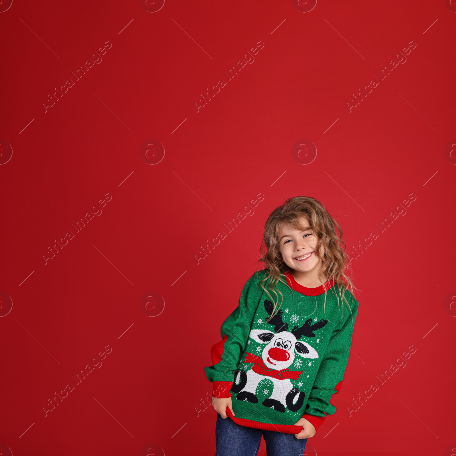 Photo of Cute little girl in green Christmas sweater smiling against red background