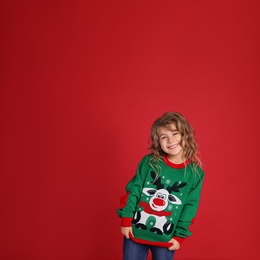 Photo of Cute little girl in green Christmas sweater smiling against red background