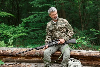 Photo of Man with hunting rifle sitting on fallen tree in forest. Space for text