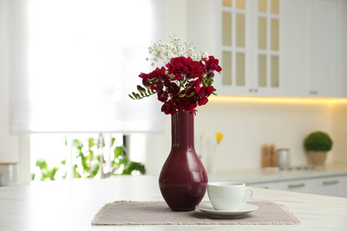 Photo of Beautiful bouquet with freesia flowers and cup on table in kitchen