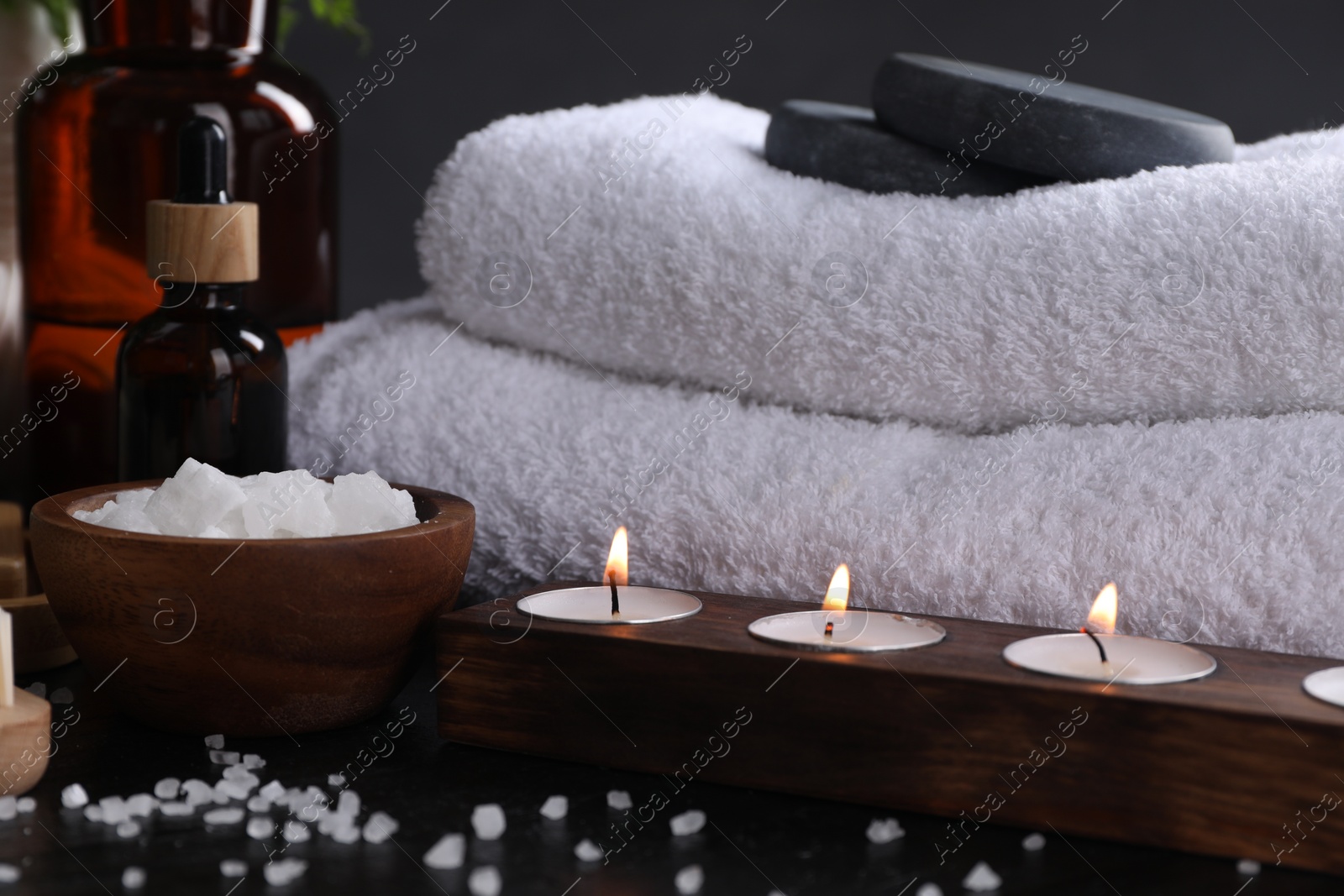 Photo of Spa composition. Sea salt, burning candles and towels on black table, closeup