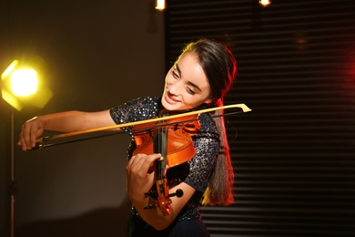 Beautiful young woman playing violin in dark room