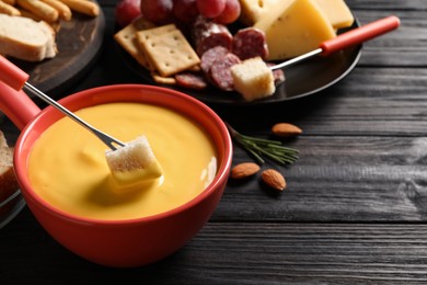 Photo of Dipping piece of bread into tasty cheese fondue at black wooden table, space for text