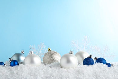 Photo of Christmas tree decoration on artificial snow against light blue background. Space for text