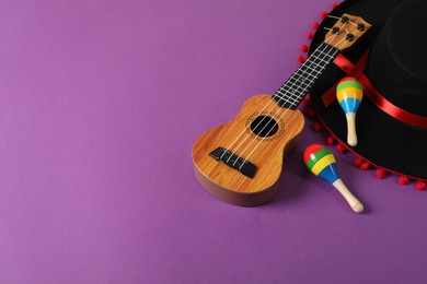 Black Flamenco hat, ukulele and maracas on purple table. Space for text