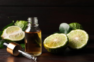 Photo of Bottle of essential oil, pipette and fresh bergamot fruits on wooden table