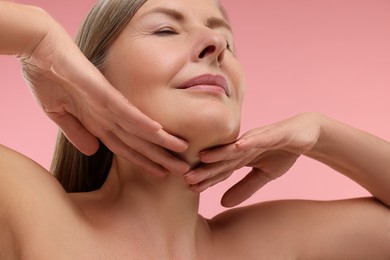 Photo of Mature woman touching her neck on pink background, low angle view