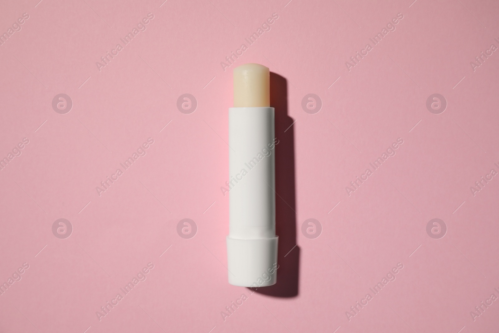 Photo of Hygienic lipstick on pink background, top view