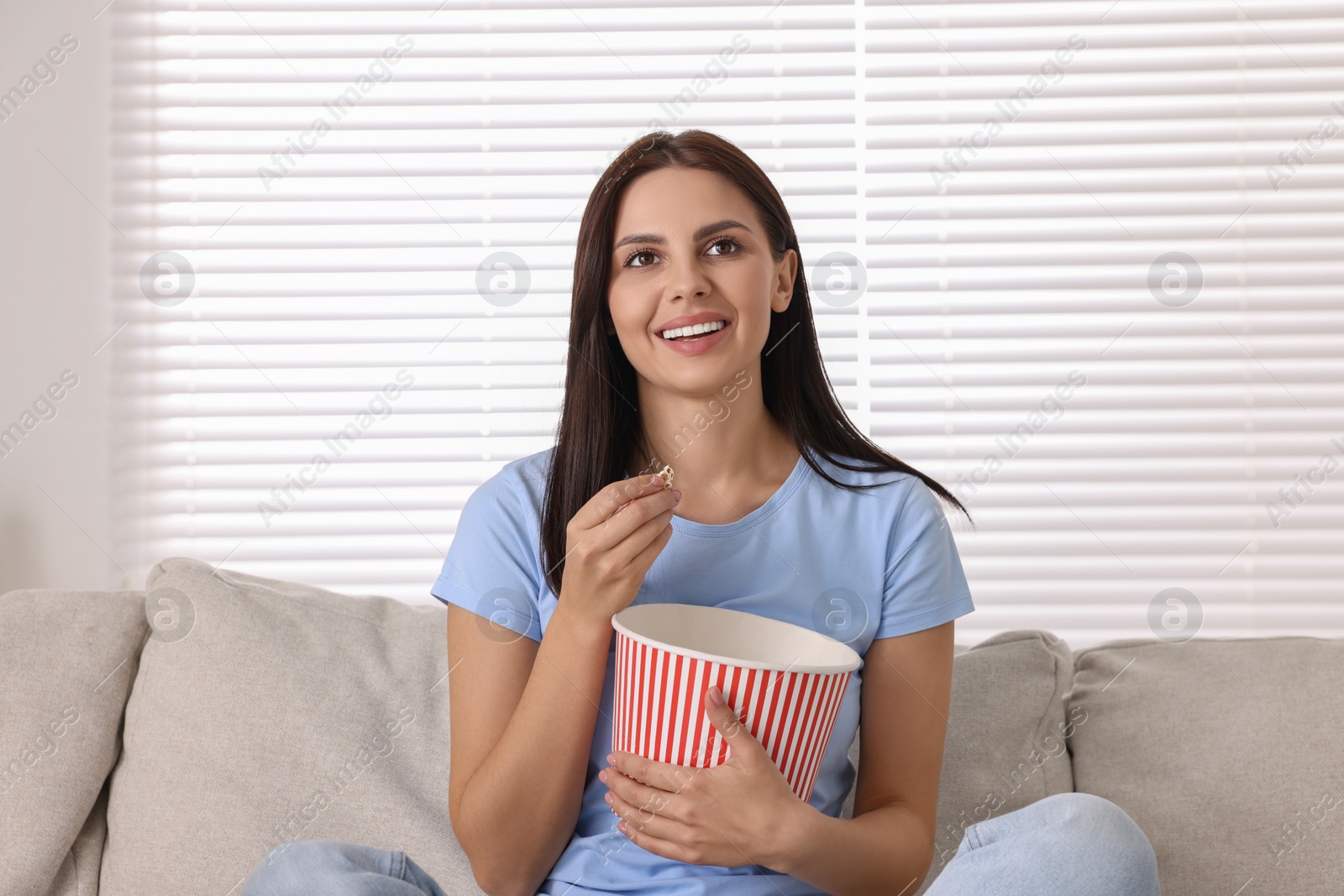 Photo of Happy woman with popcorn bucket watching TV on sofa at home