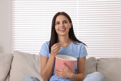 Happy woman with popcorn bucket watching TV on sofa at home