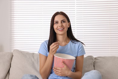 Photo of Happy woman with popcorn bucket watching TV on sofa at home