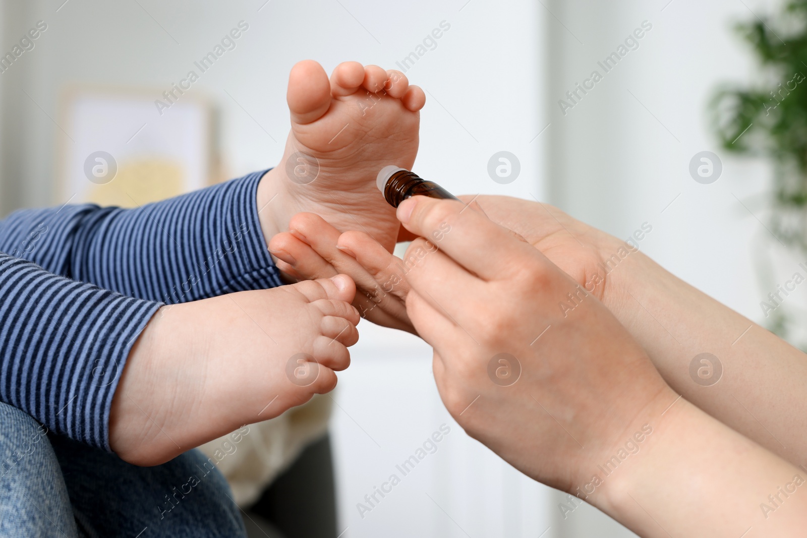 Photo of Mother applying essential oil from roller bottle onto her baby`s heel indoors, closeup