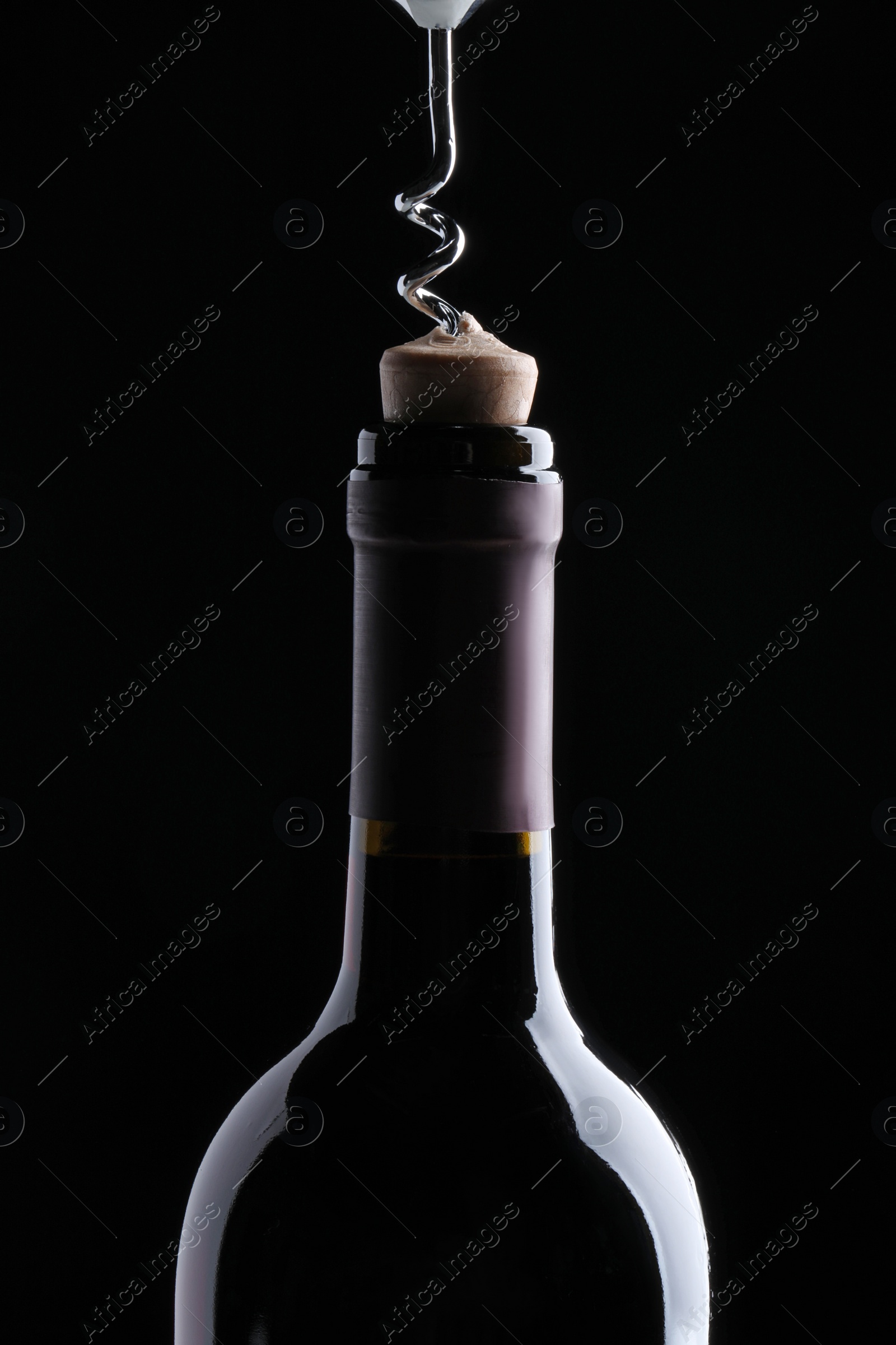 Photo of Opening wine bottle with corkscrew on dark background, closeup