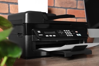 Photo of Modern printer with paper near computer on wooden desk at home