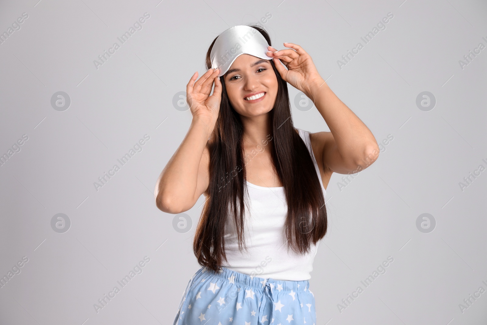 Photo of Beautiful woman wearing sleeping mask on light grey background. Bedtime