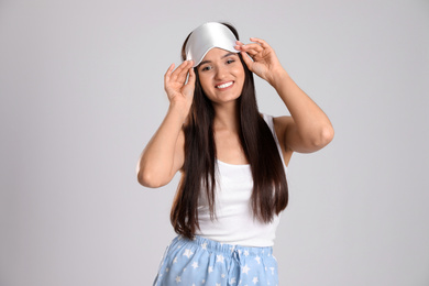 Beautiful woman wearing sleeping mask on light grey background. Bedtime