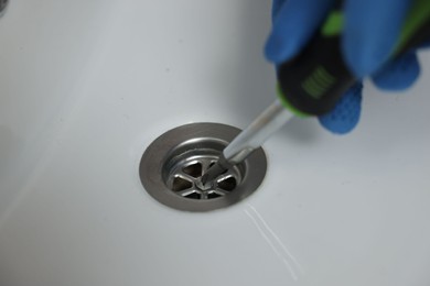 Photo of Plumber in gloves repairing sink with screwdriver, closeup