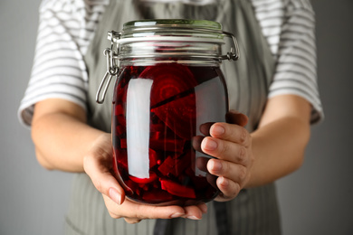 Photo of Woman holding glass jar with pickled beets, closeup