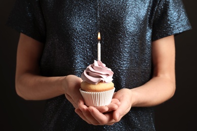 Woman holding delicious birthday cupcake with burning candle, closeup