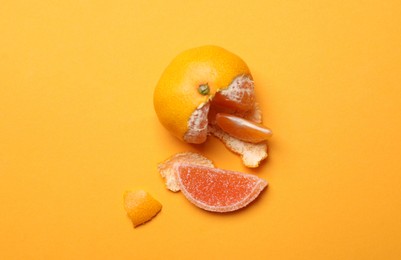 Photo of Fresh tangerine with one jelly candy as its segment on orange background, flat lay. April Fools' Day