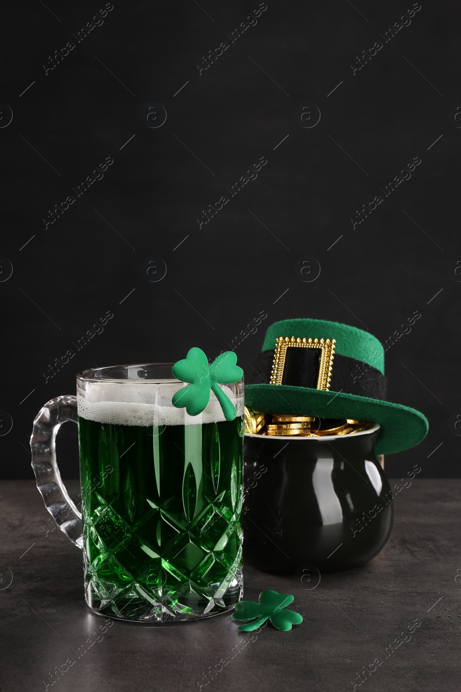 Photo of St. Patrick's day celebration. Green beer, leprechaun hat, pot of gold and decorative clover leaves on grey table. Space for text