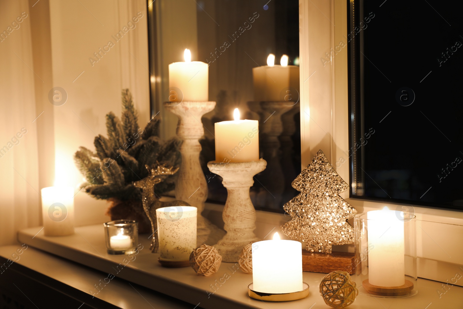 Photo of Burning candles and Christmas decor on window sill at night