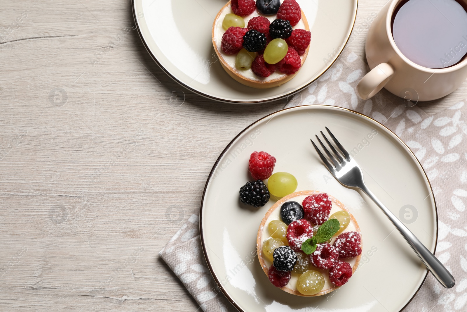 Photo of Delicious tartlets with berries and tea on light wooden table, flat lay. Space for text