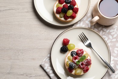 Delicious tartlets with berries and tea on light wooden table, flat lay. Space for text