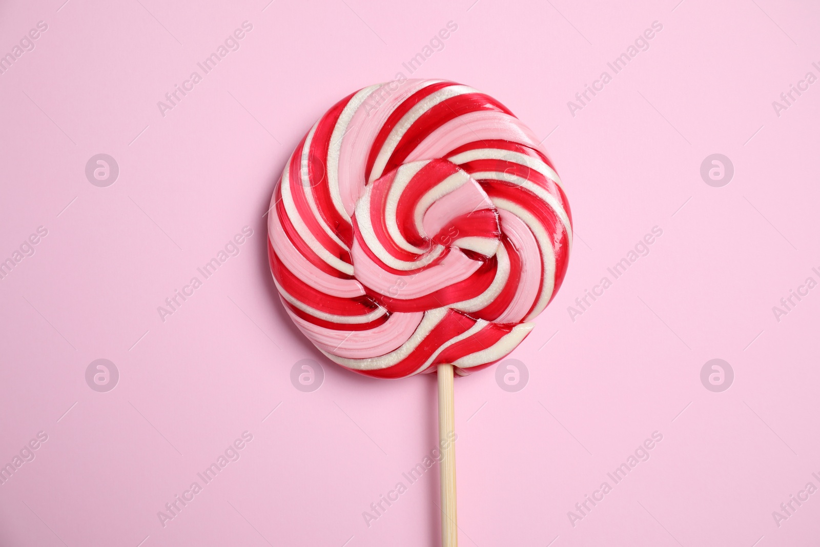 Photo of Stick with colorful lollipop swirl on pink background, top view