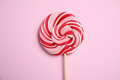 Photo of Stick with colorful lollipop swirl on pink background, top view