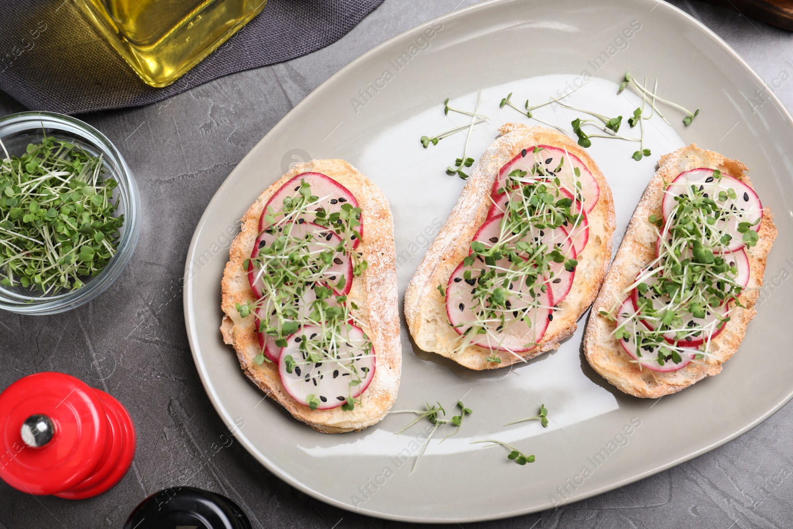 Photo of Delicious sandwiches with radish, cheese and microgreens on grey table, flat lay