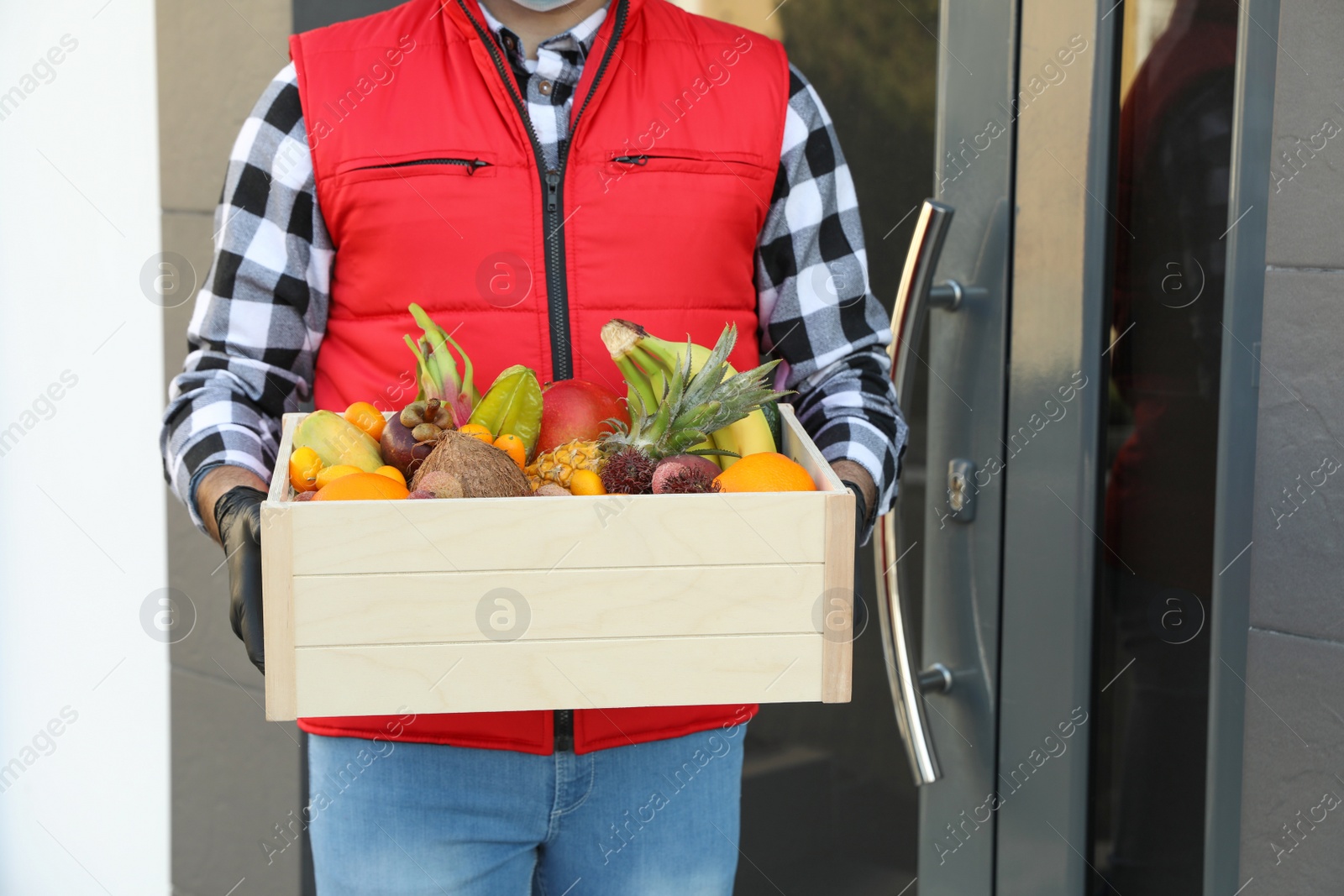 Photo of Courier holding crate with assortment of exotic fruits outdoors, closeup