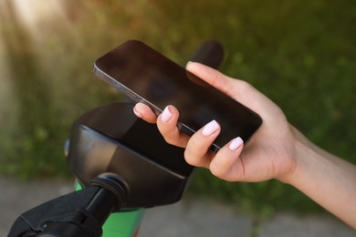 Photo of Woman using smartphone to pay and unblock electric kick scooter outdoors, closeup