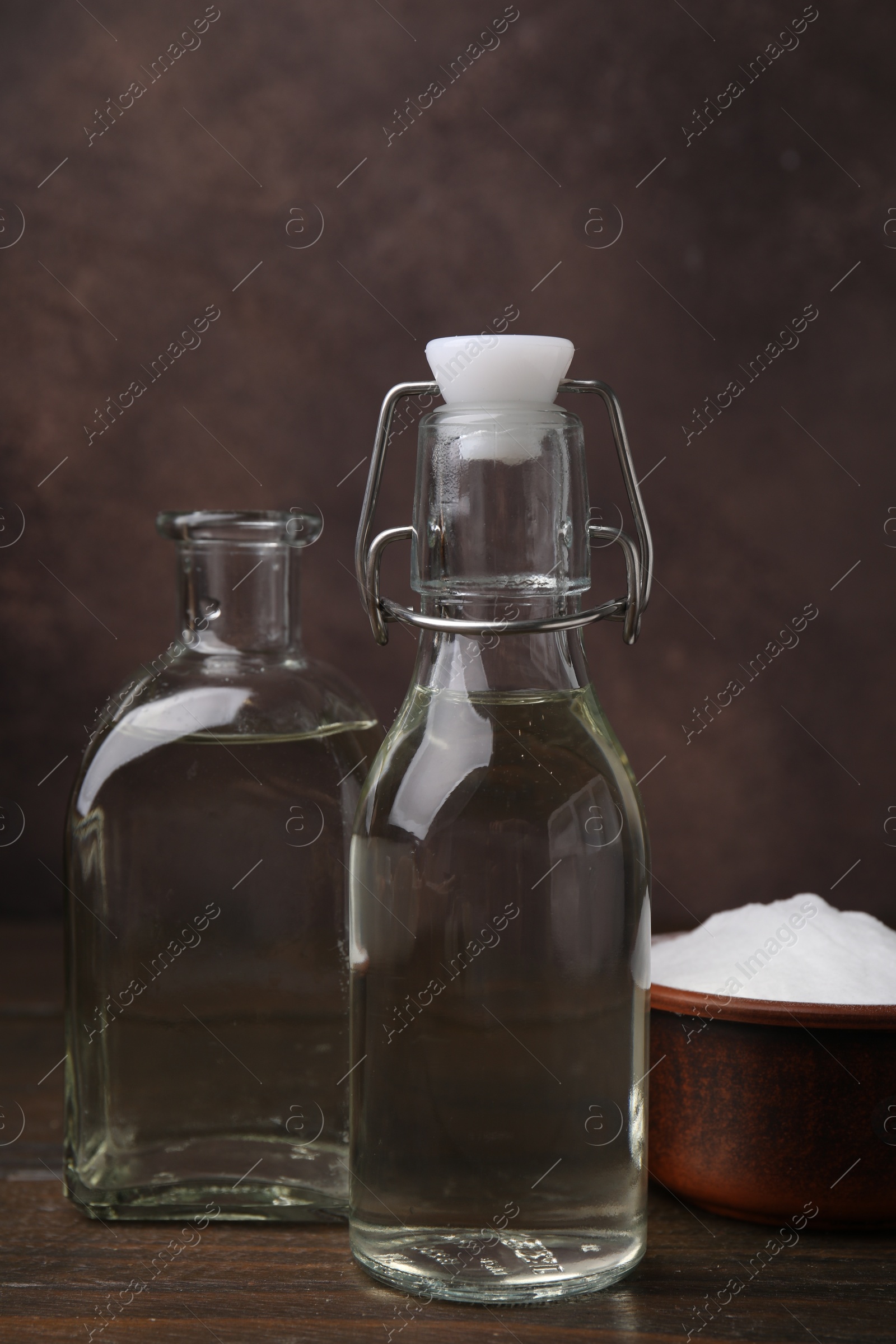 Photo of Vinegar in glass bottles and baking soda on wooden table