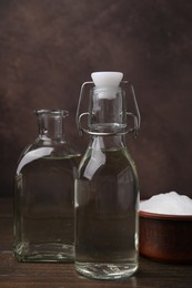 Photo of Vinegar in glass bottles and baking soda on wooden table