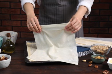 Photo of Woman making delicious baklava at wooden table, closeup