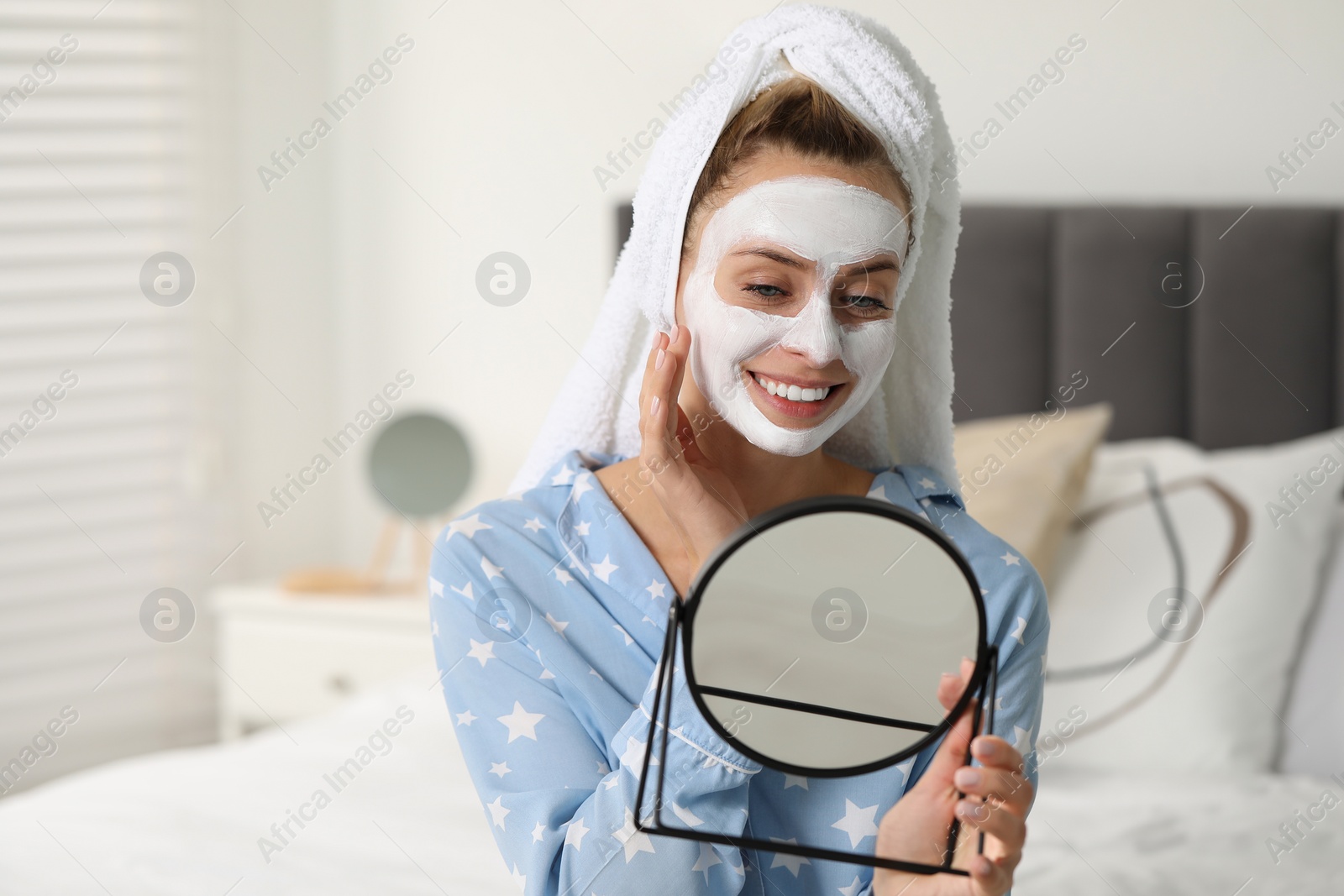 Photo of Young woman with face mask looking into mirror in bedroom, space for text. Spa treatments