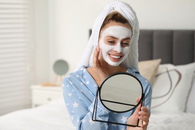 Photo of Young woman with face mask looking into mirror in bedroom, space for text. Spa treatments