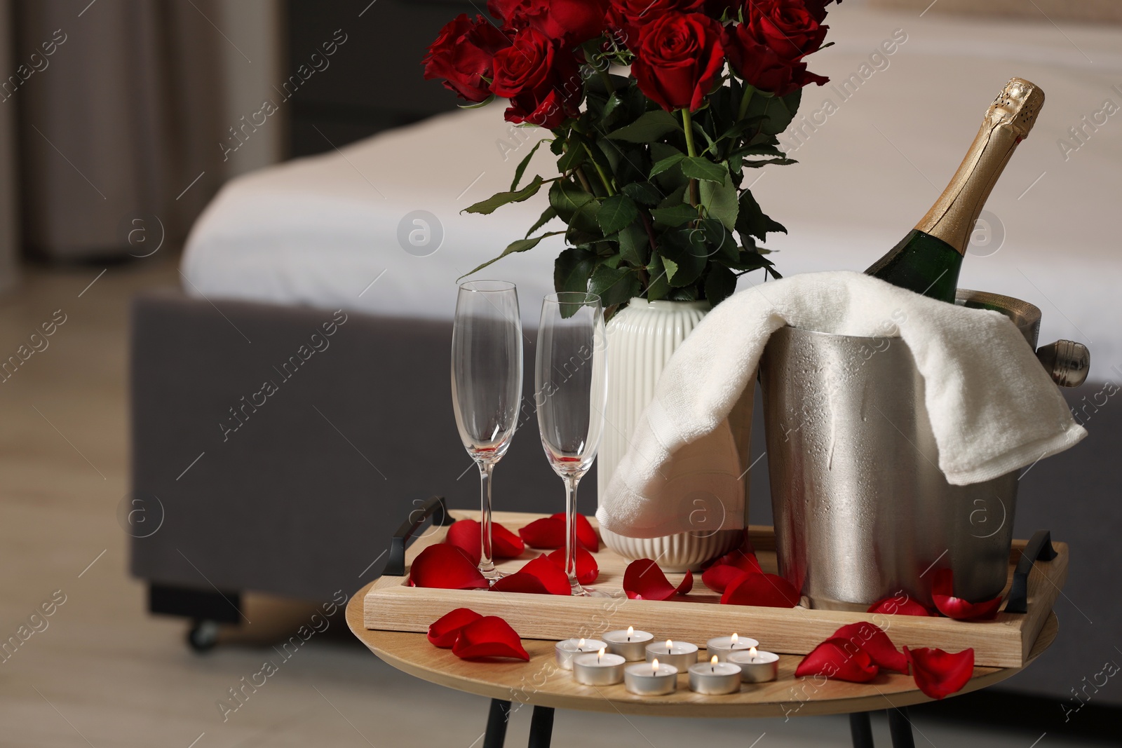 Photo of Honeymoon. Sparkling wine, glasses and bouquet of roses on wooden table in room. Space for text