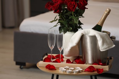Photo of Honeymoon. Sparkling wine, glasses and bouquet of roses on wooden table in room. Space for text