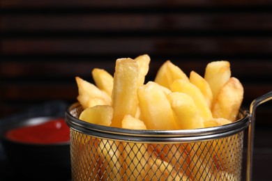 Photo of Frying basket with tasty french fries on blurred background, closeup