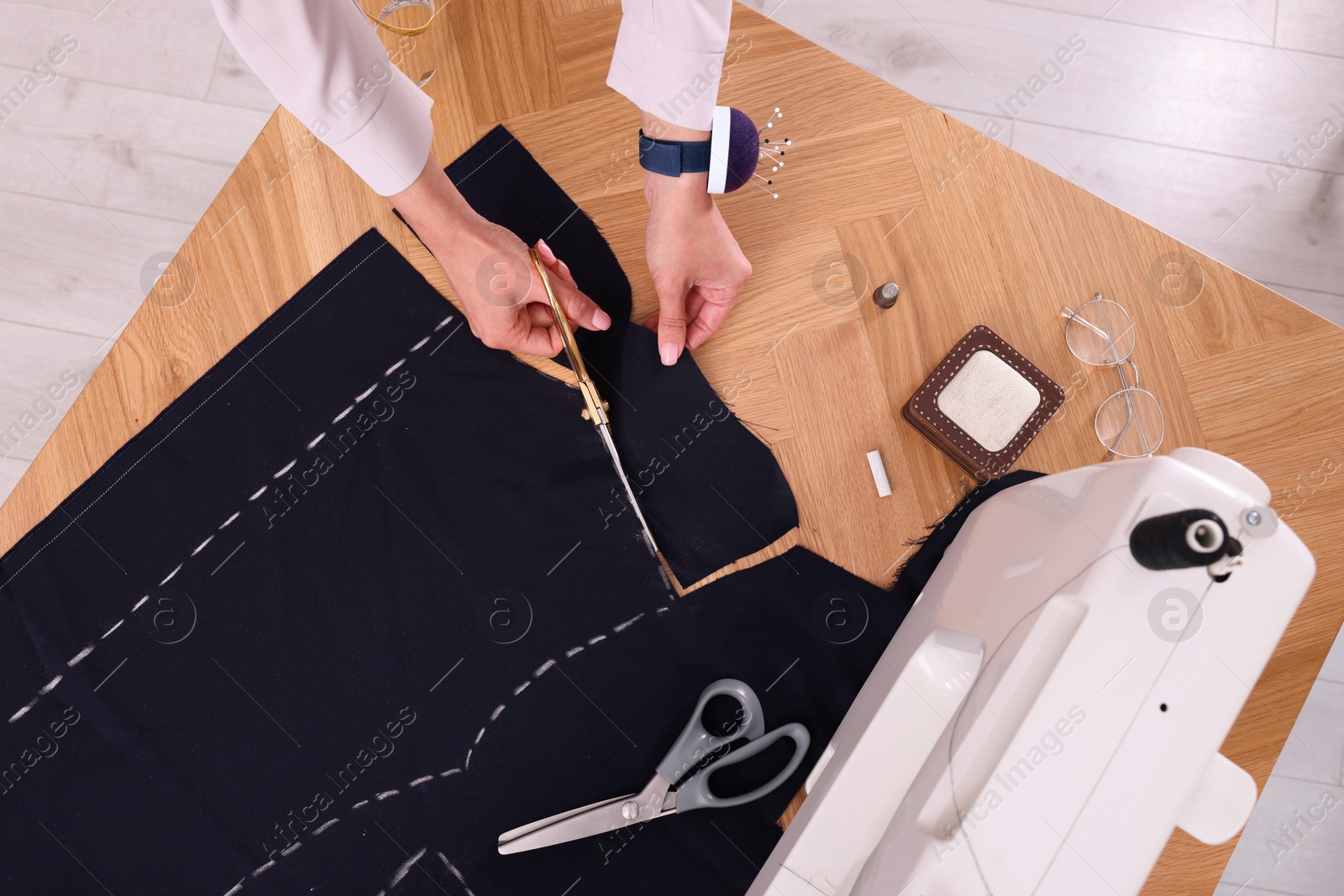 Photo of Dressmaker cutting fabric by following chalked sewing pattern in workshop, top view