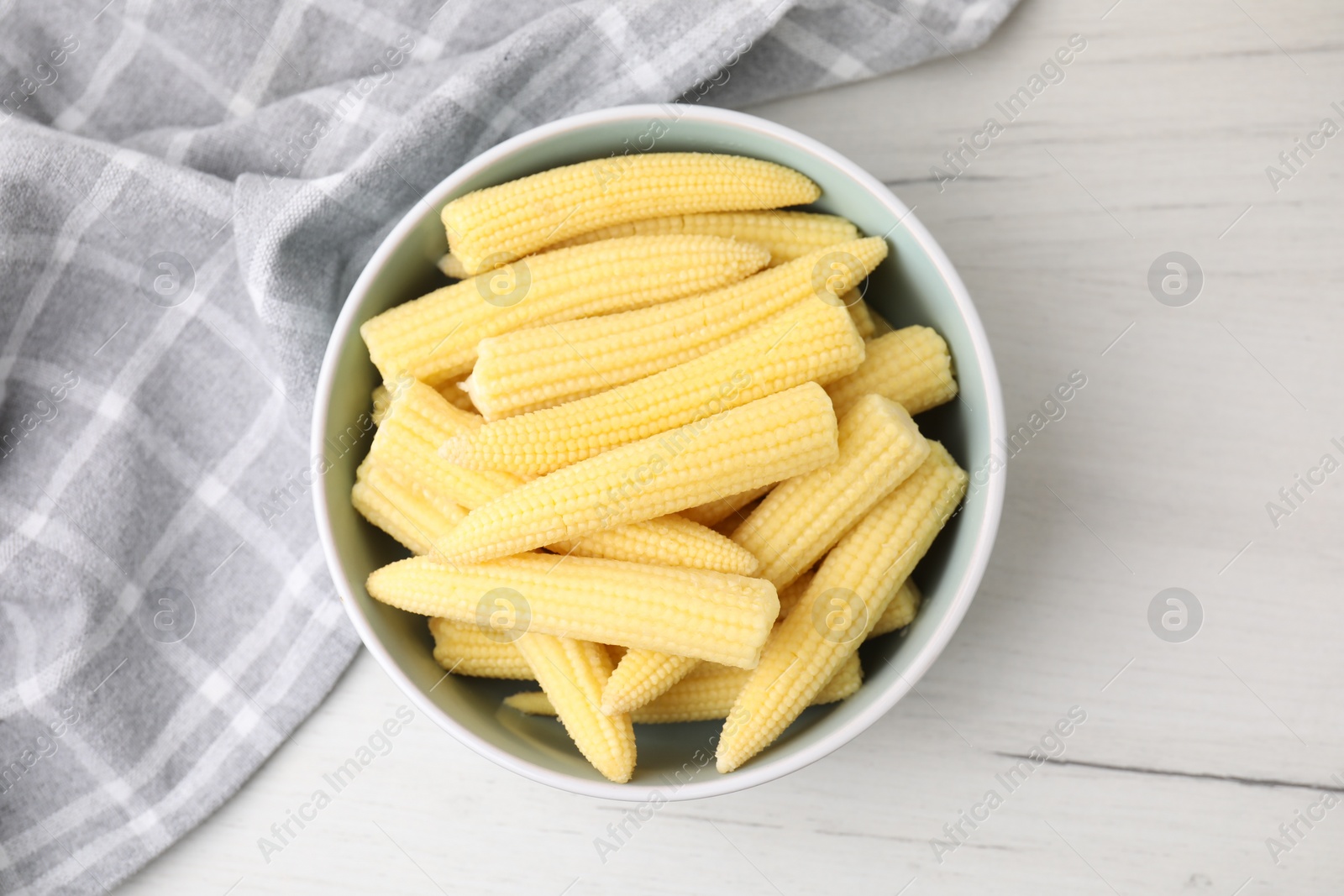 Photo of Tasty fresh yellow baby corns in bowl on white wooden table, top view