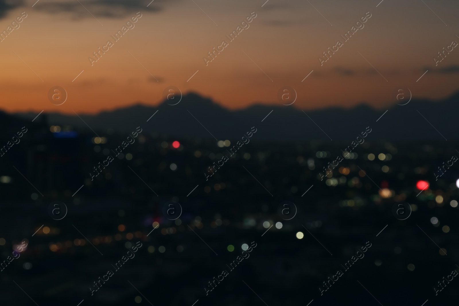 Photo of Blurred view of sunset with dark clouds above big mountains and night city
