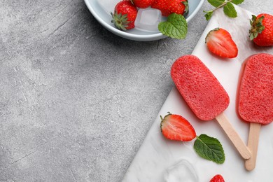 Photo of Tasty fruit ice pops with strawberries on grey table, flat lay. Space for text