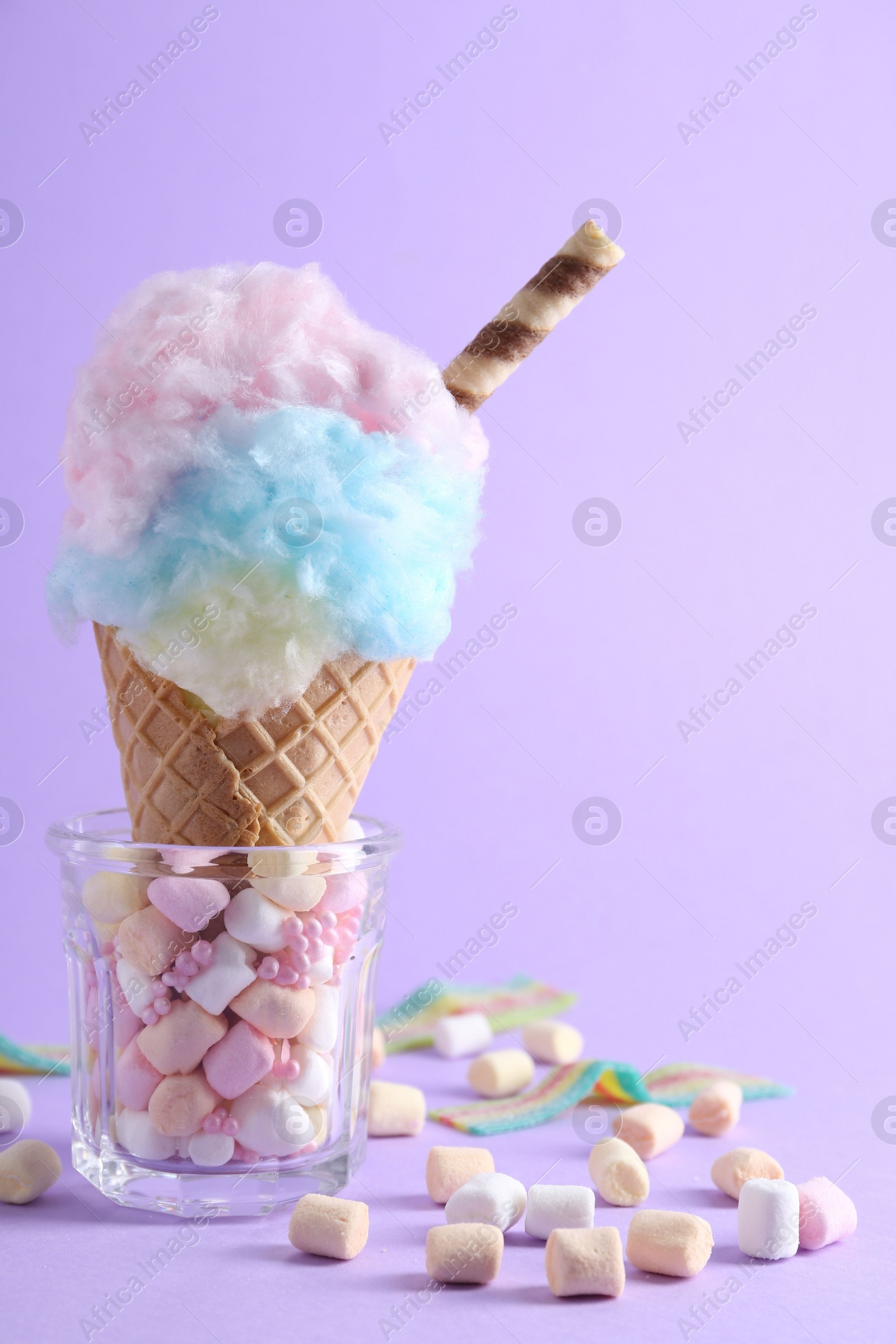 Photo of Sweet cotton candy in waffle cone and marshmallows on purple background