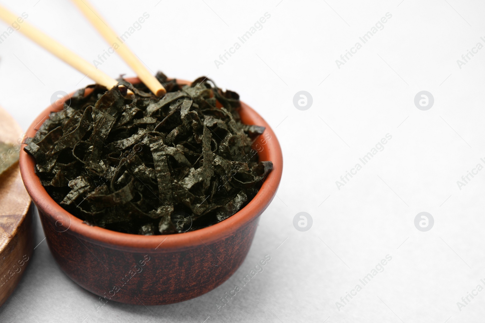 Photo of Bowl with chopped nori sheets and chopsticks on white table, closeup. Space for text
