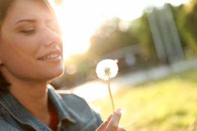 Young woman with dandelion in park on sunny day, closeup. Allergy free concept