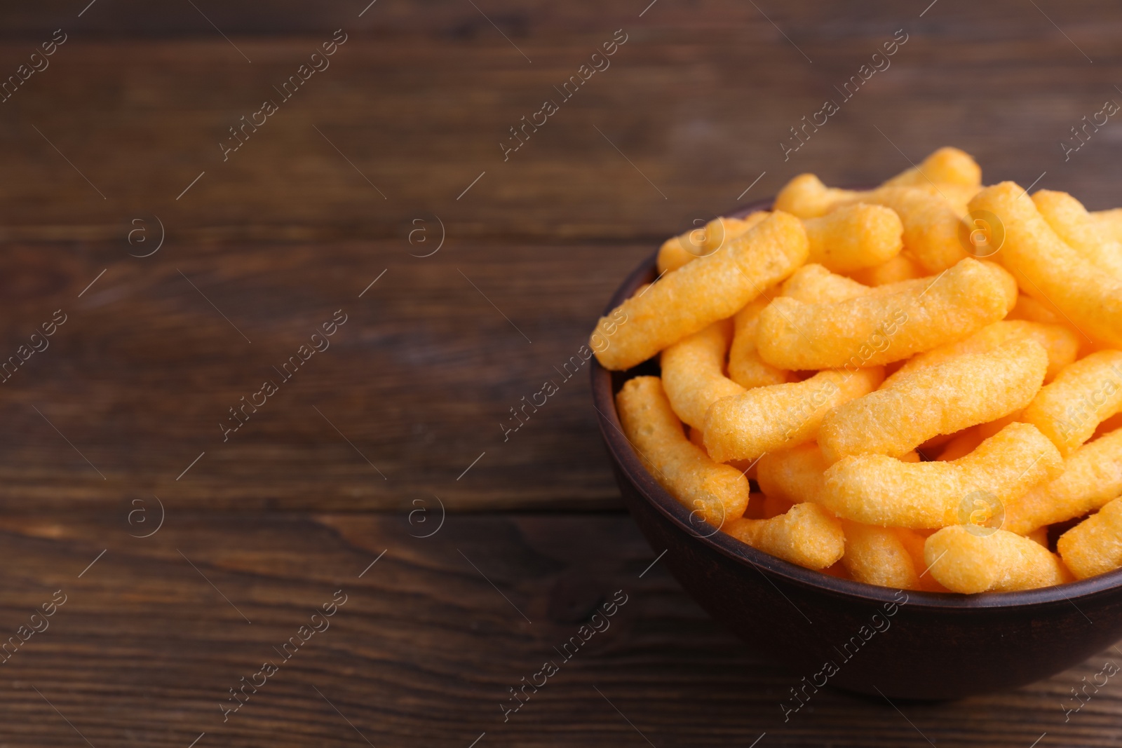 Photo of Bowl with crunchy cheesy corn snack on wooden table, closeup. Space for text