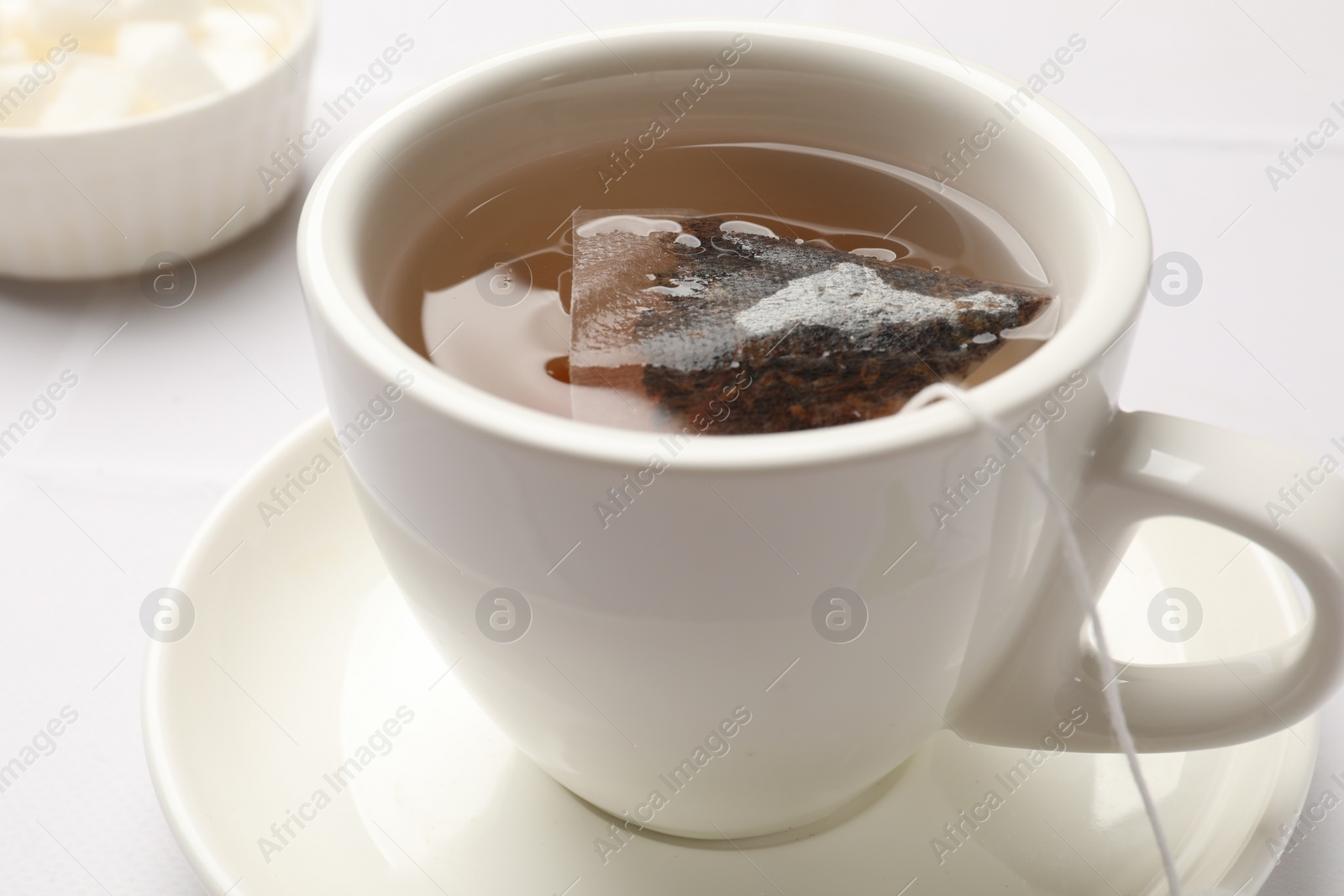 Photo of Tea bag in cup with hot drink on white table, closeup